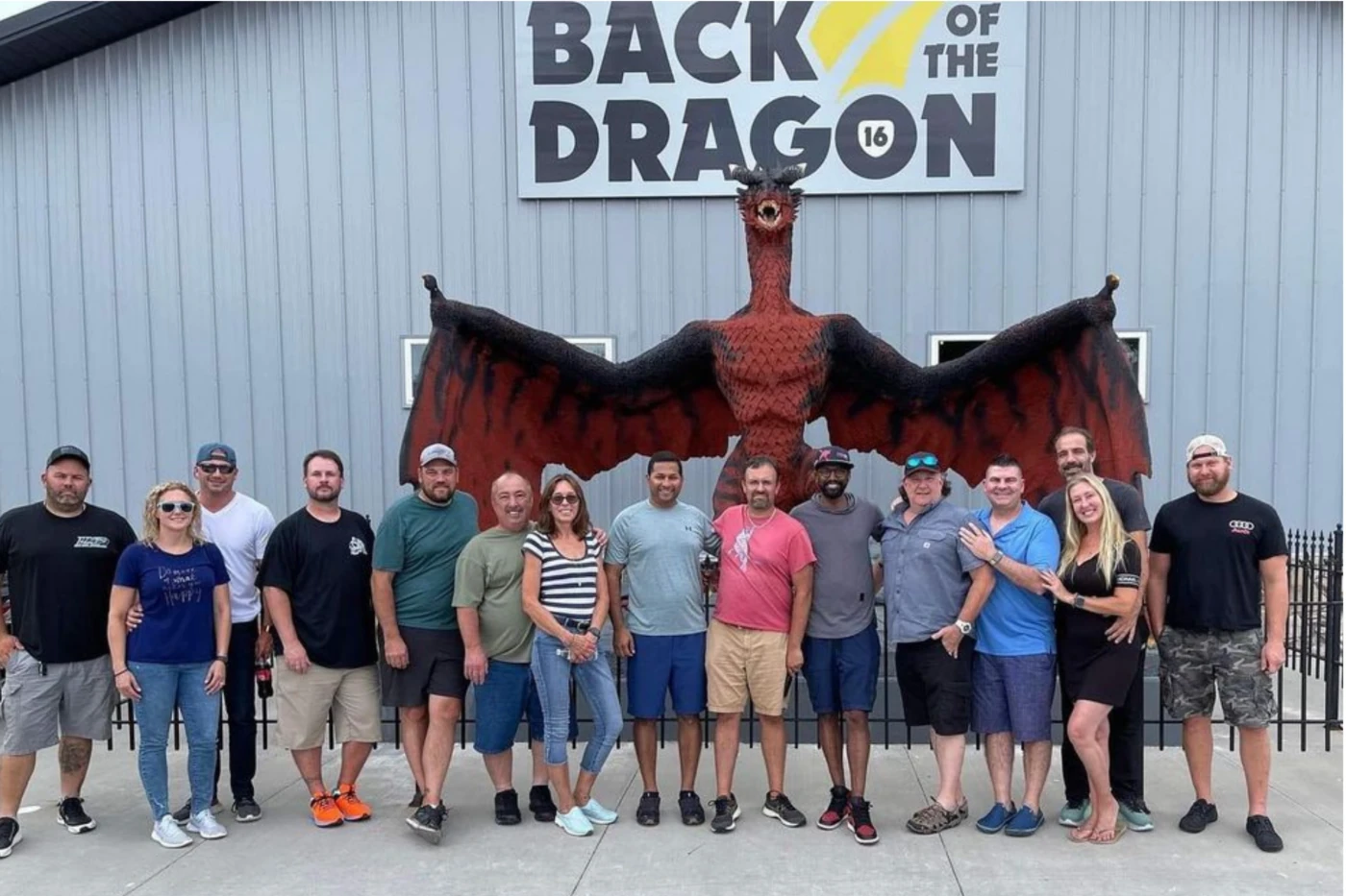 Group of visitors pose beneath a giant red dragon statue with wings spread at the “Back of the Dragon” attraction, smiling outdoors.